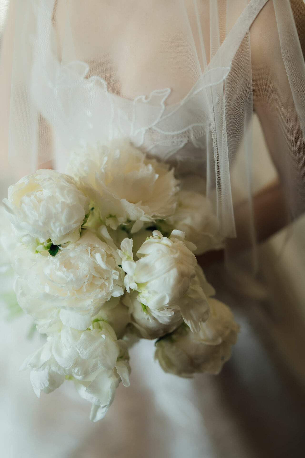 Bride holding white peonies, soft romantic focus.