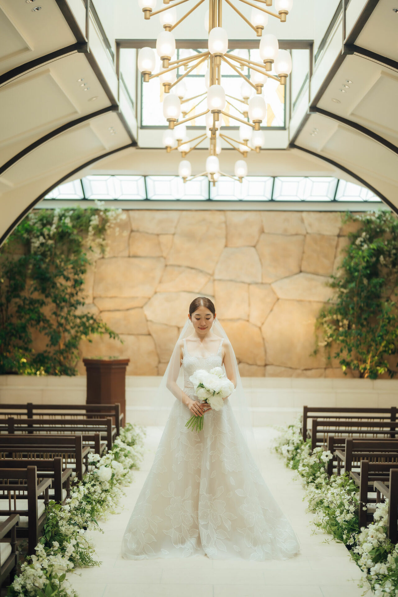 Bride in chapel aisle holding white bouquet.