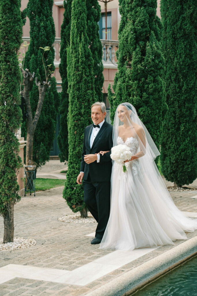 Katya Ruiz in couture gown walks arm-in-arm outdoors.