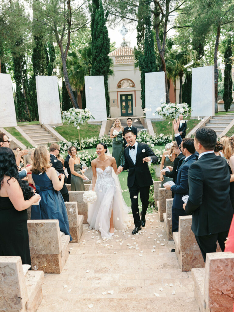 Joyful bride and groom exit amid petals and cheers.