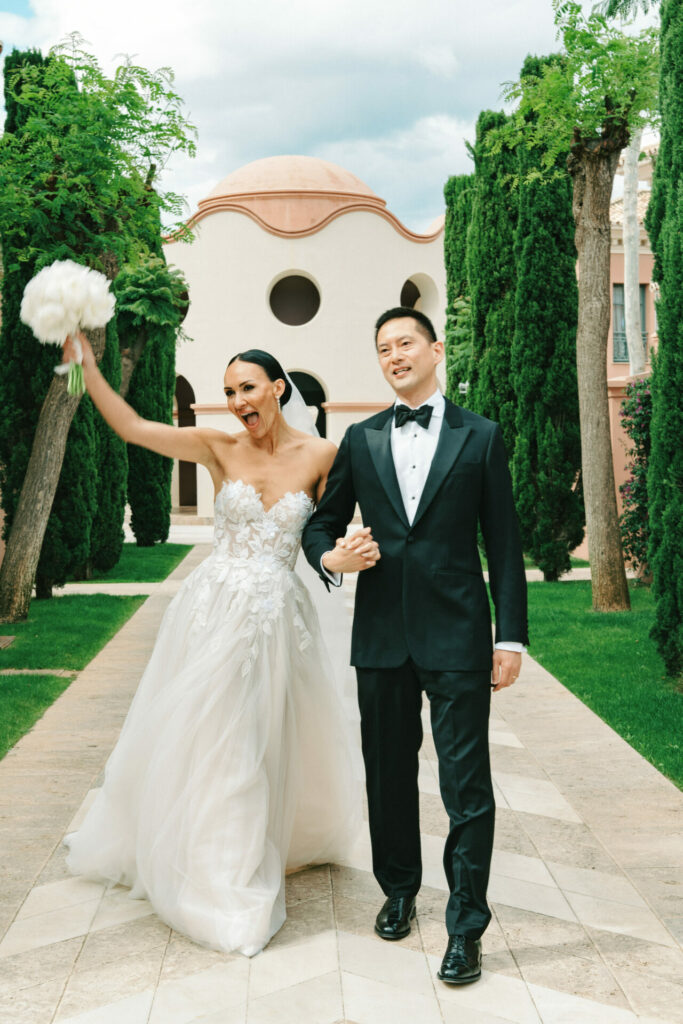 Katya Ruiz and groom walk, she lifts bouquet, smiling.