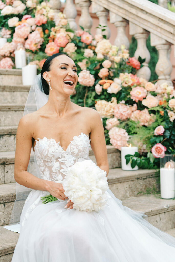 Bride in strapless gown on steps, bouquet, vibrant flowers.