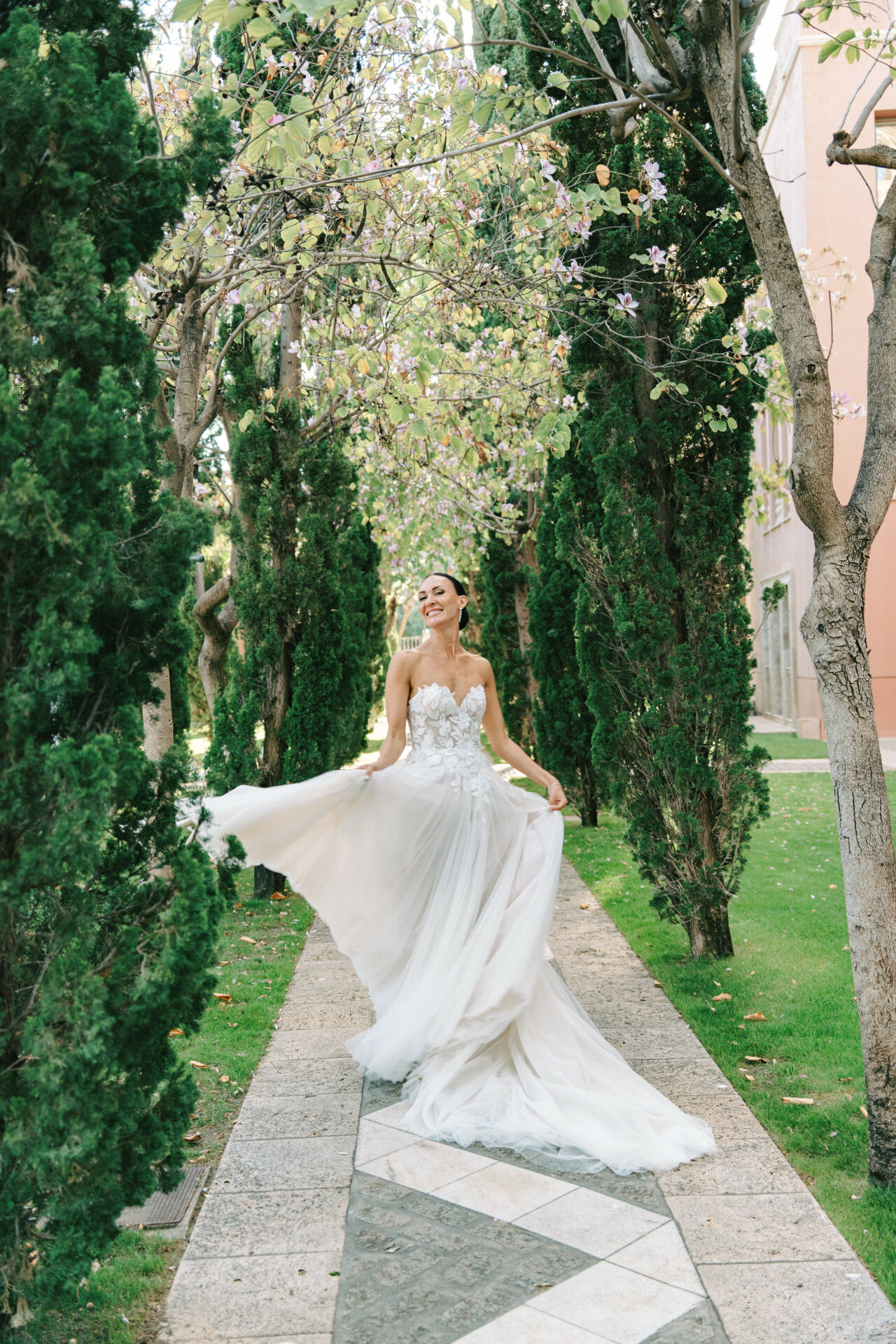 Smiling bride in Mira Zwillinger gown on garden path.