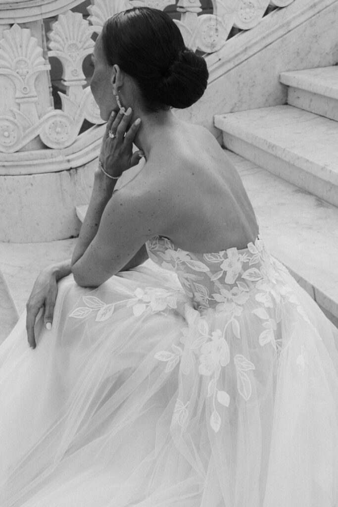 Katya Ruiz in lace gown on marble stairs, gazing away.