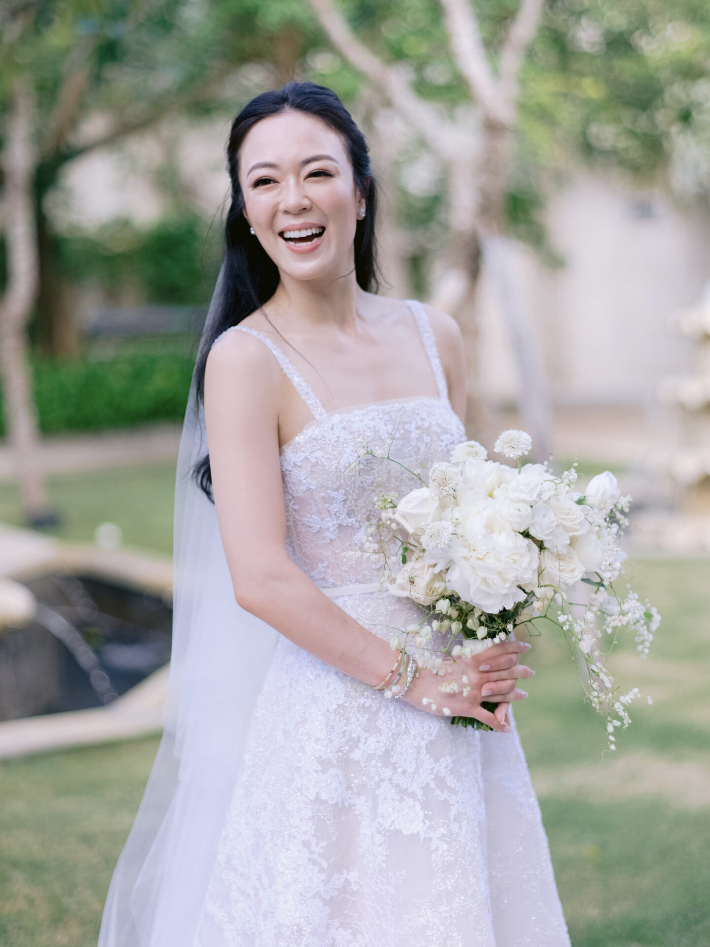 Bride in lacy dress holds bouquet outdoors.