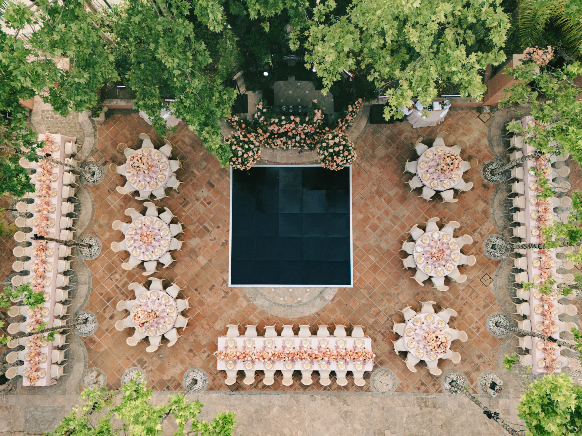 Outdoor event with white tables, black dance floor, greenery.
