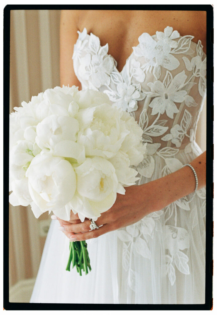 Katya Ruiz in white floral lace gown, holding peonies.