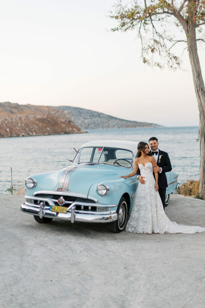 Bride and groom by vintage blue car near seaside.