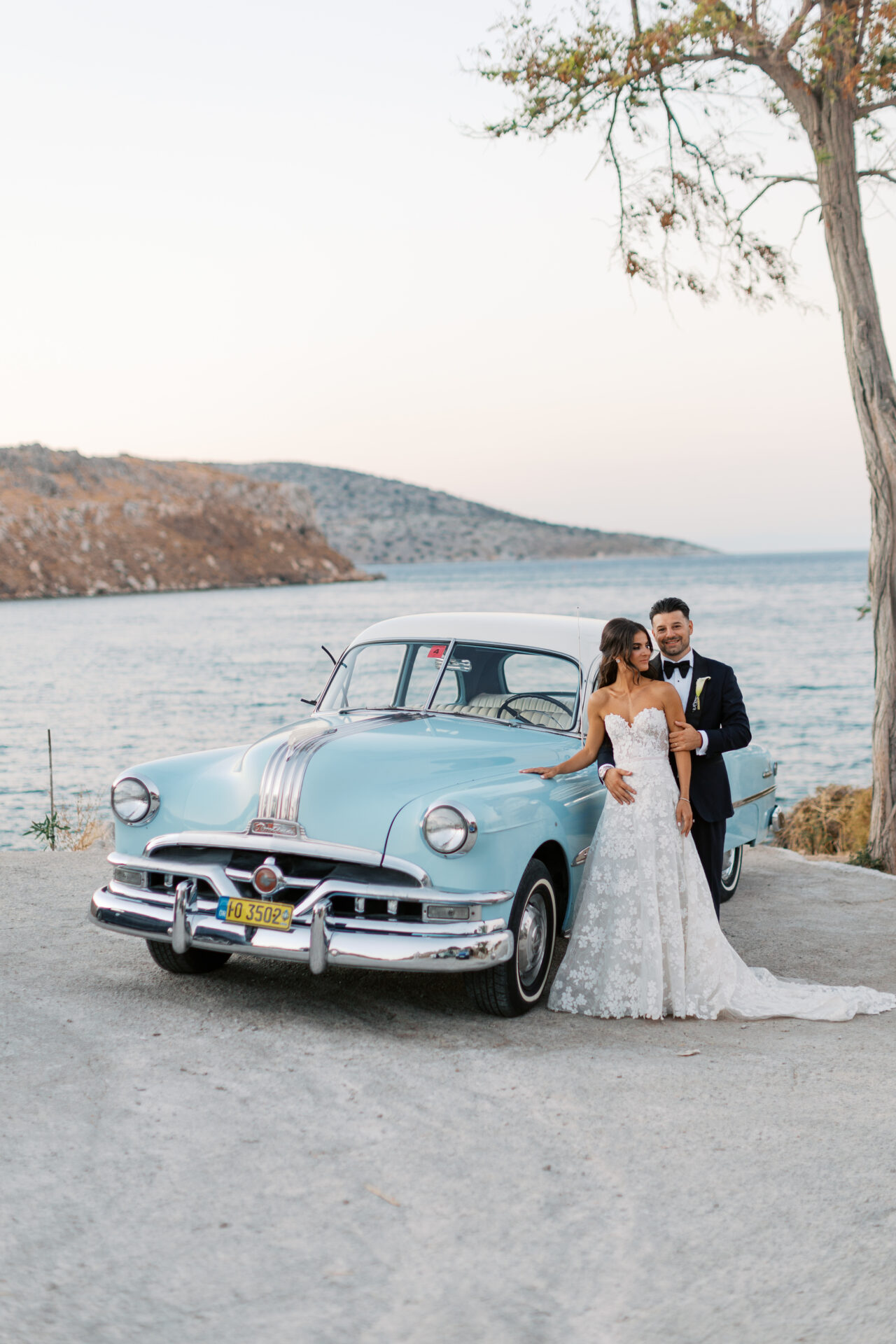 Bride and groom by vintage blue car near seaside.
