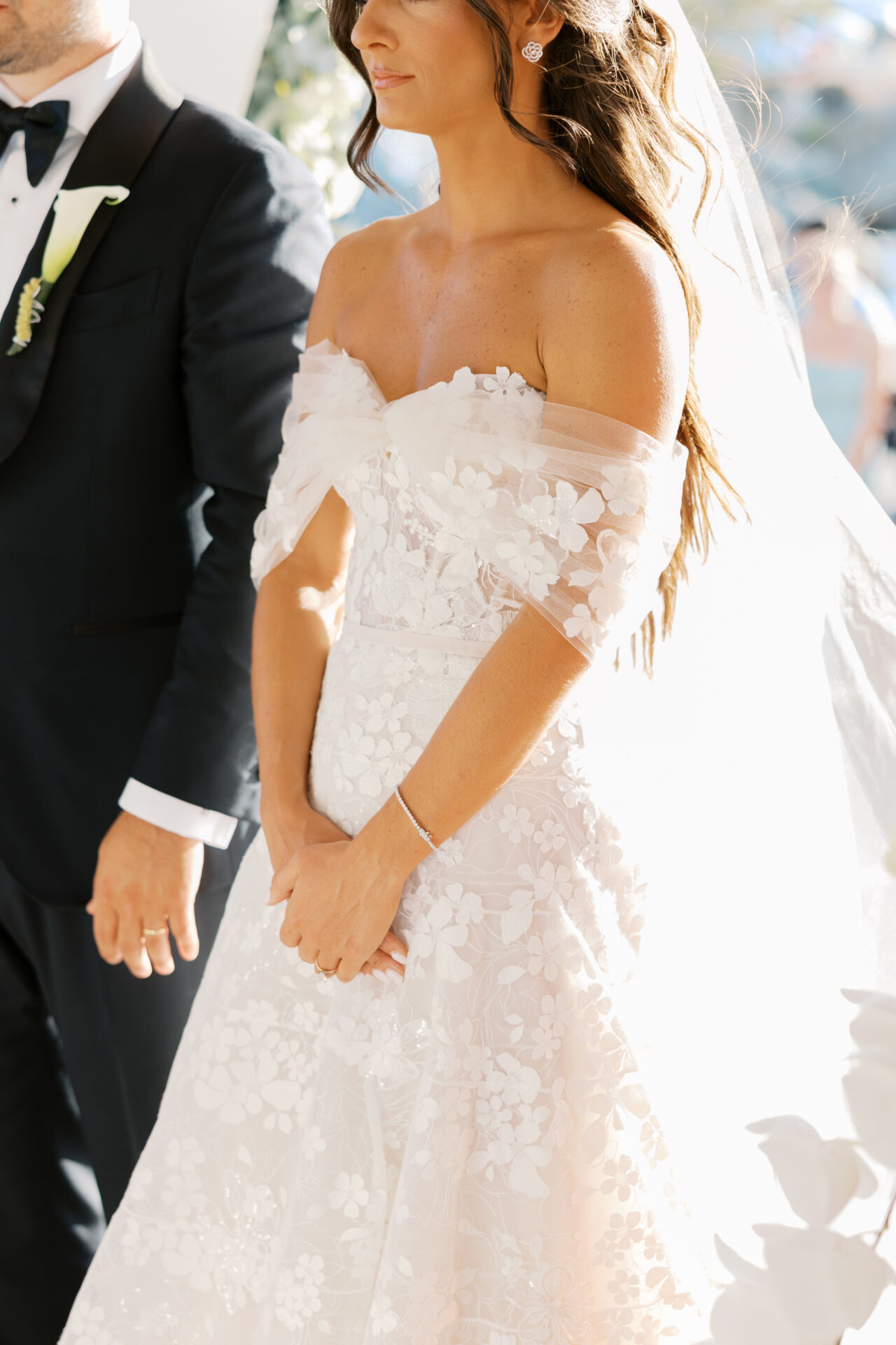 Bride in floral lace gown with groom, sunlit hair.