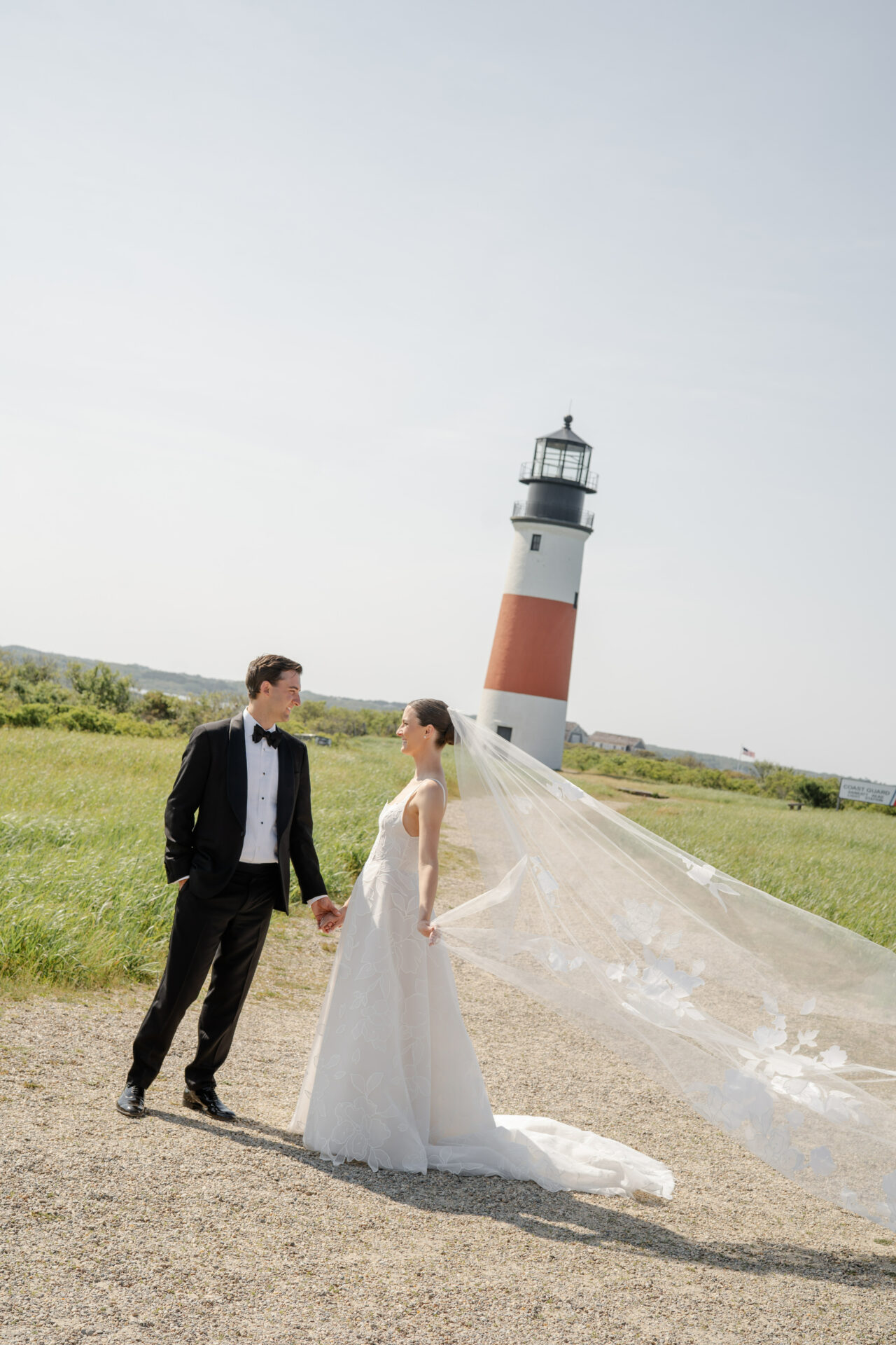 Bride and groom by lighthouse, veil blowing.