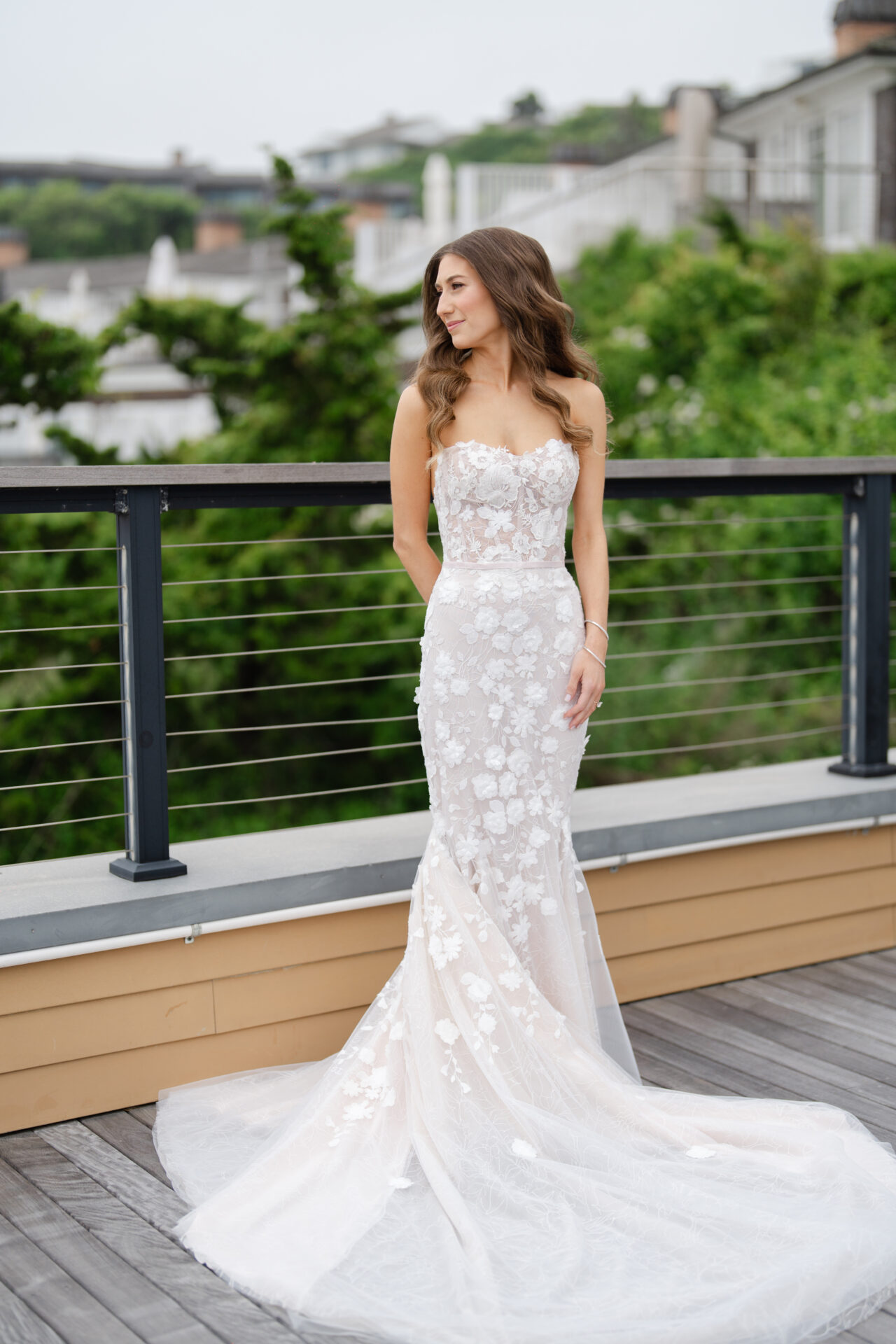 Woman in lace mermaid gown on deck, greenery behind.
