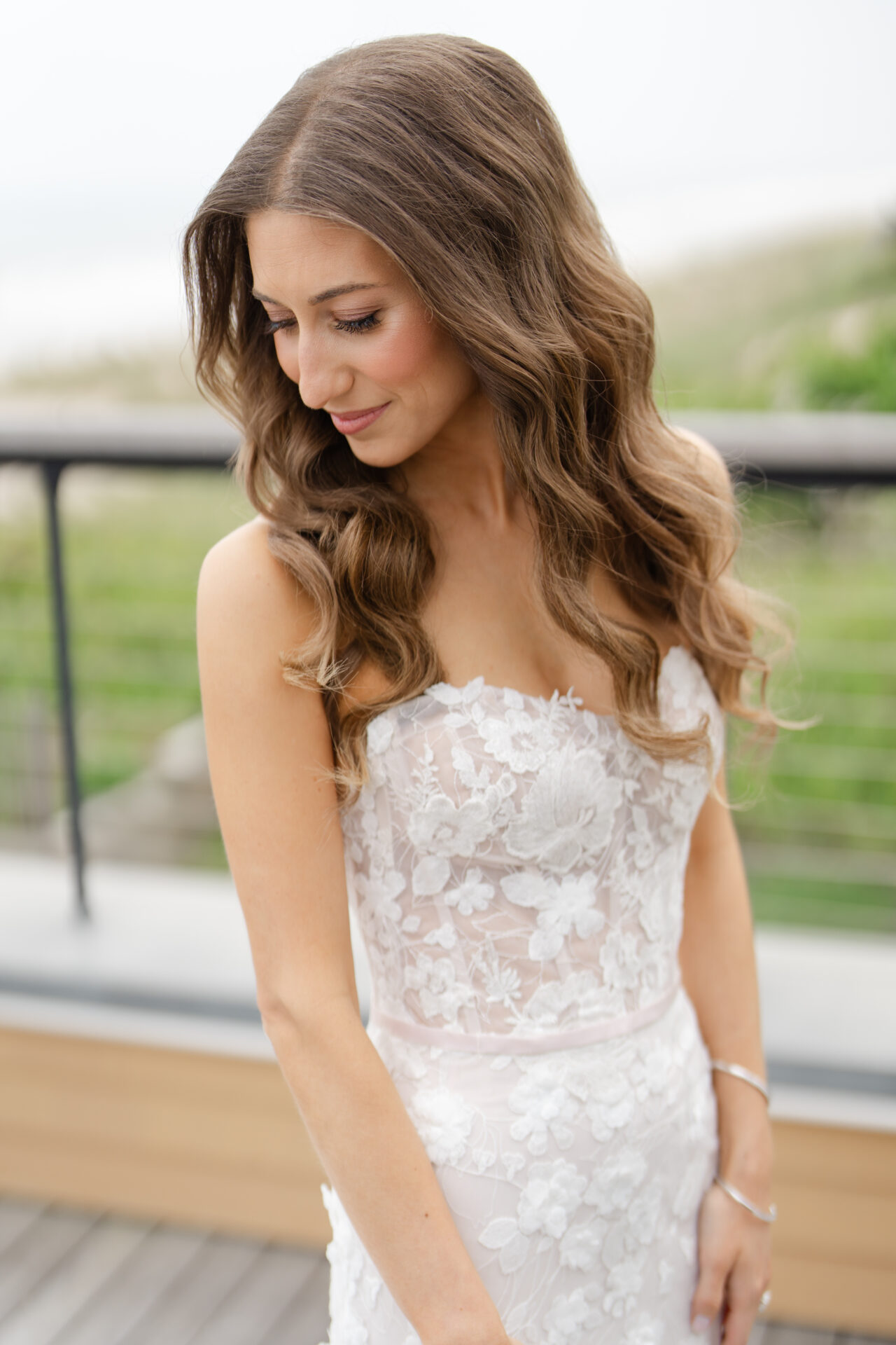Smiling woman in strapless lace wedding dress outdoors.