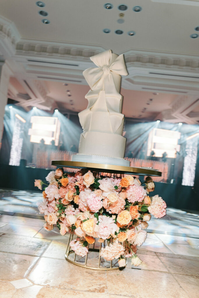 Elegant white tiered cake with bow, pink flowers.