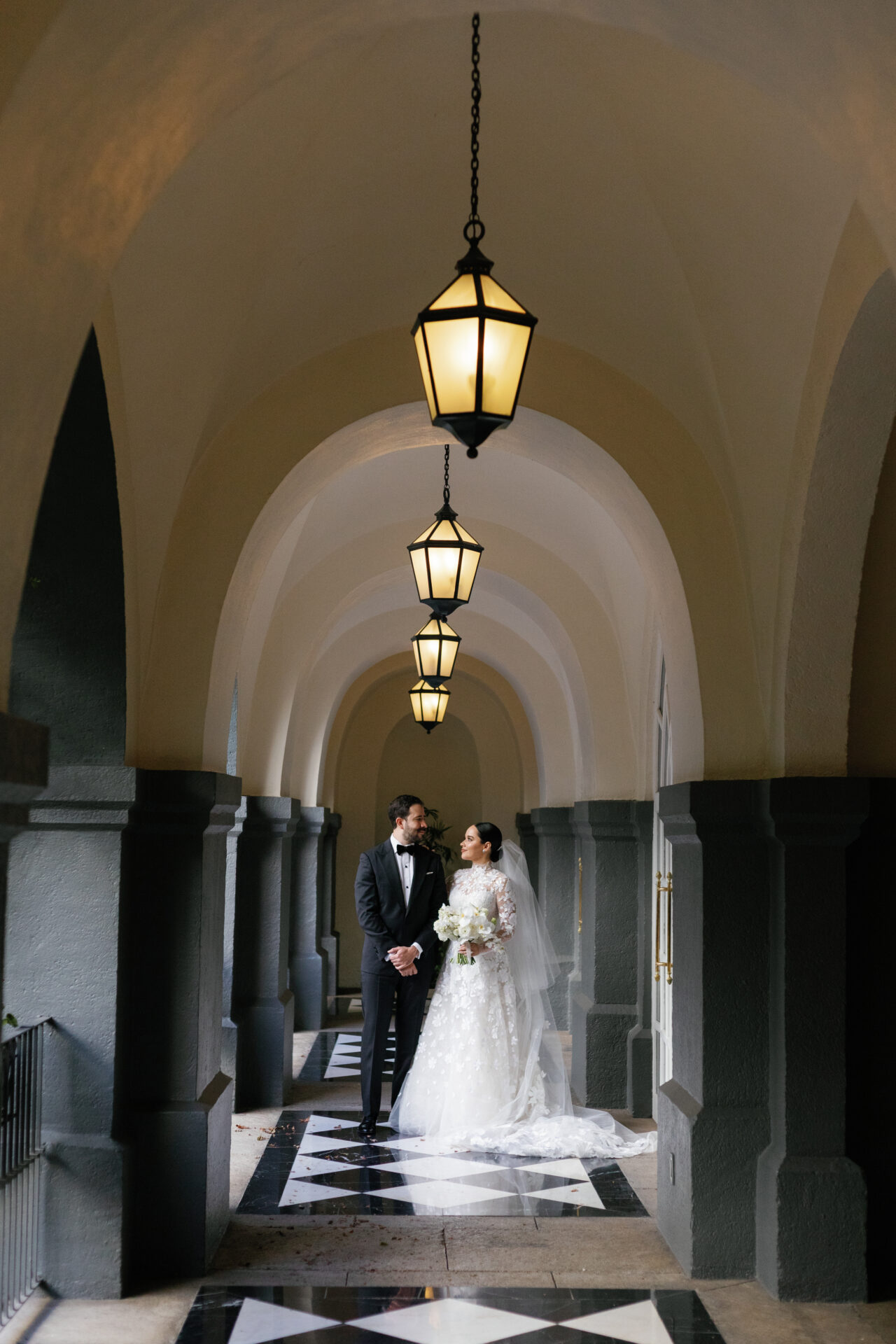 Bride and groom under ornate arches, gazing lovingly.