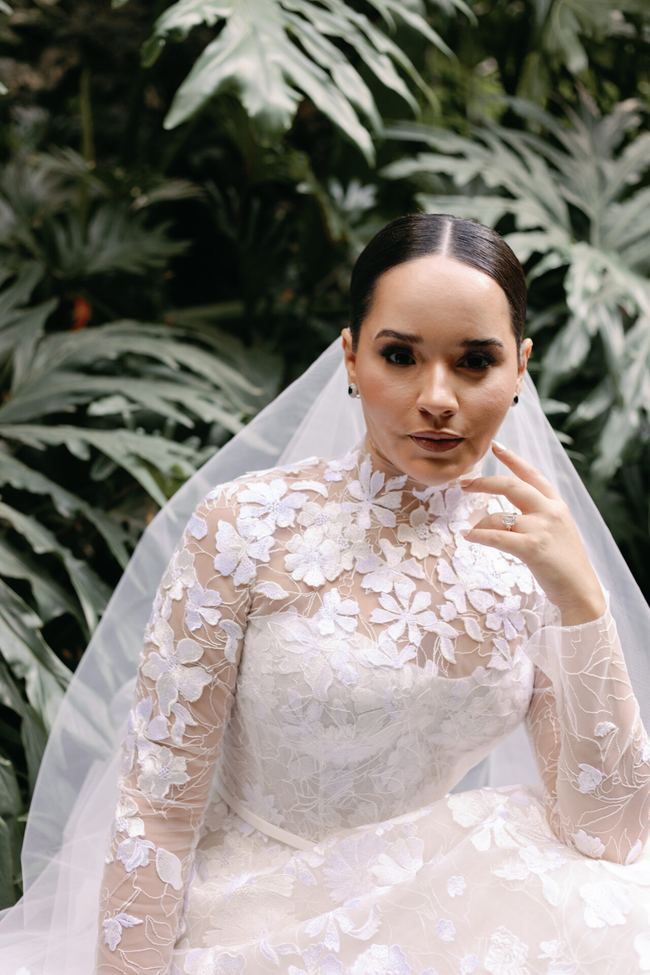 Bride in lace dress poses by green leaves.