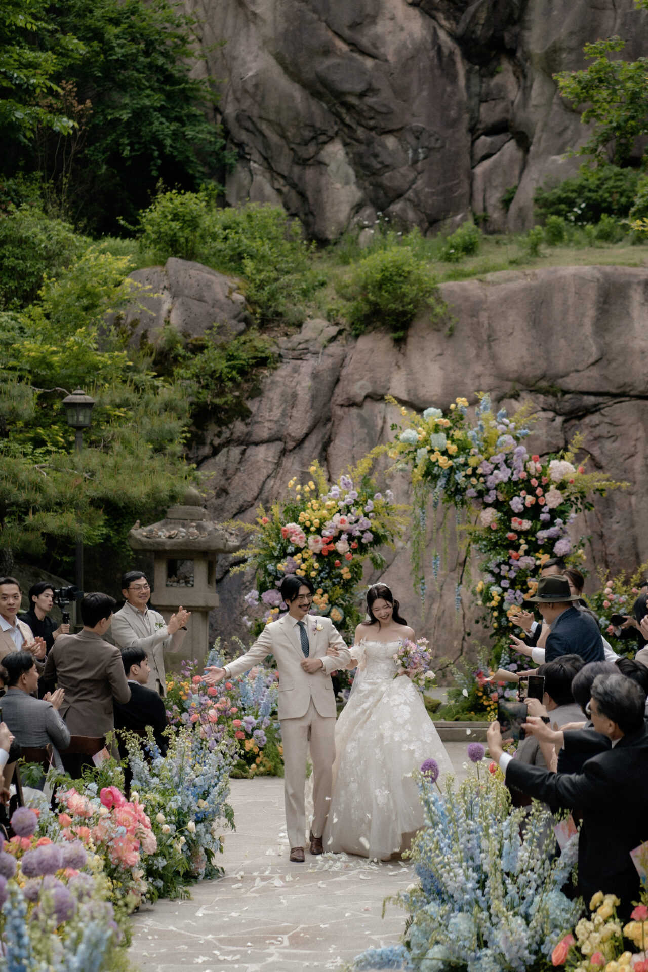 Newlyweds walk aisle amid cheering guests outdoors.