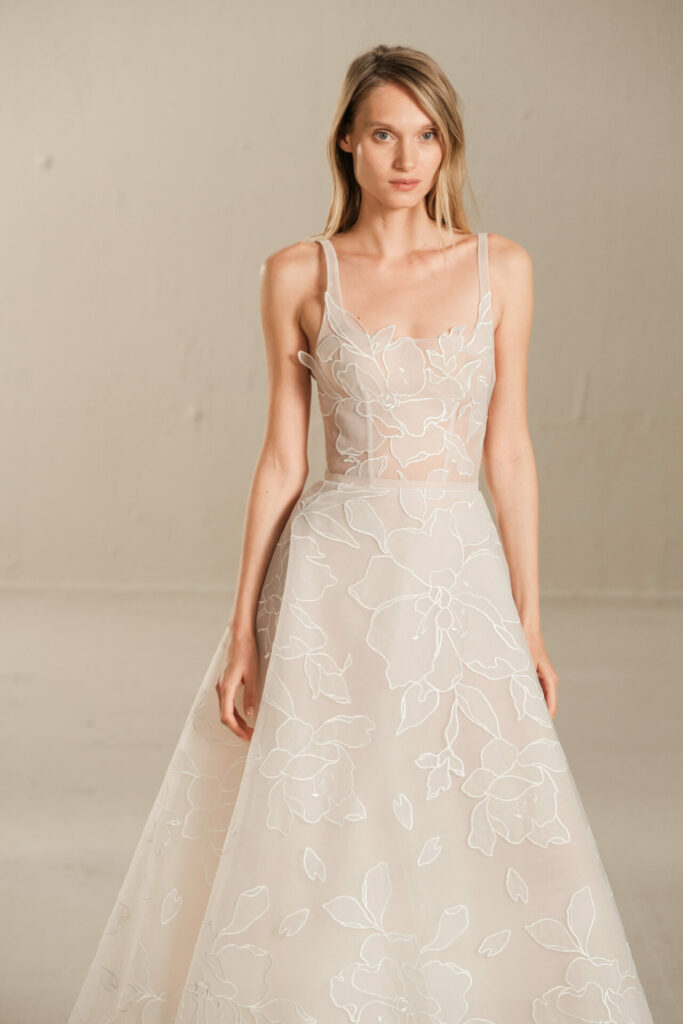 Woman in sheer floral-embroidered dress standing.