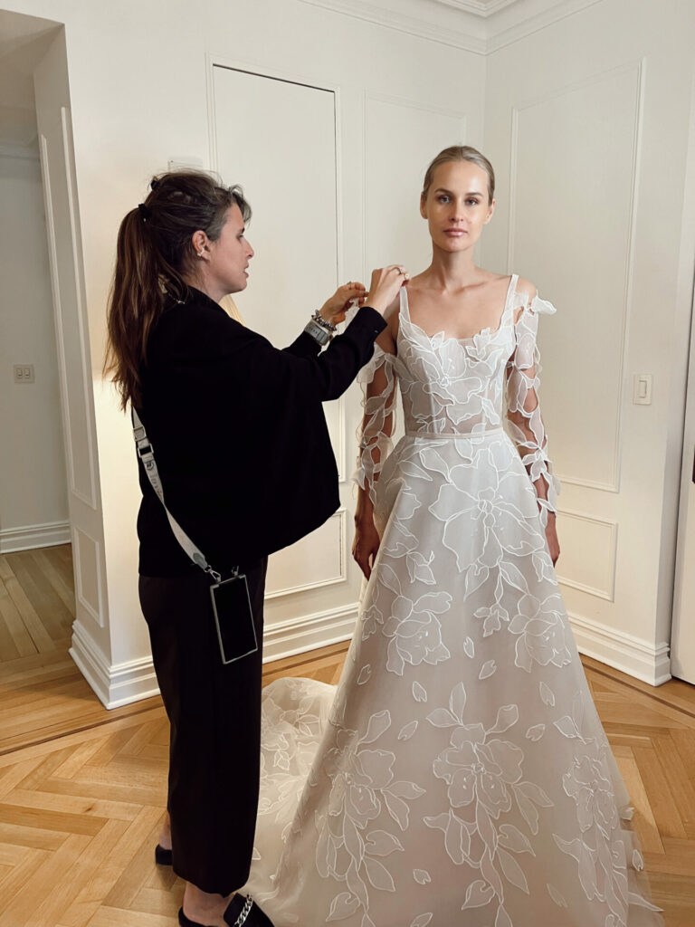 Woman adjusts anothers floral wedding dress straps.