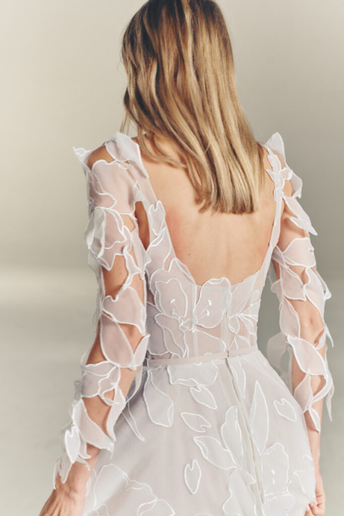 Woman in sheer white floral dress, neutral background.
