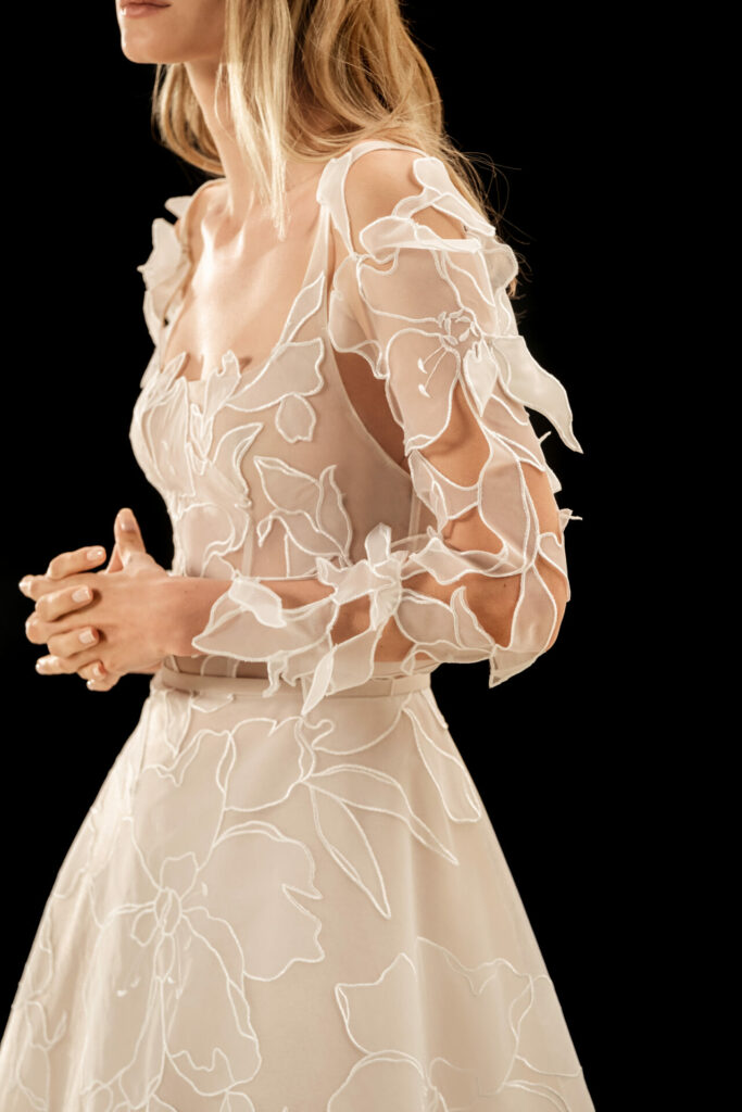 Woman in sheer floral dress, clasped hands.