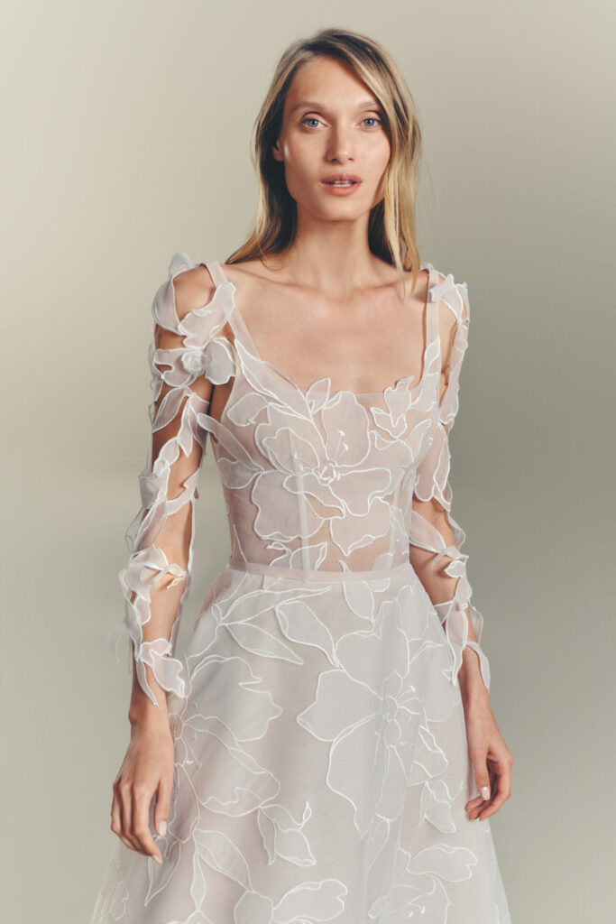 Woman in sheer floral white dress, neutral background.