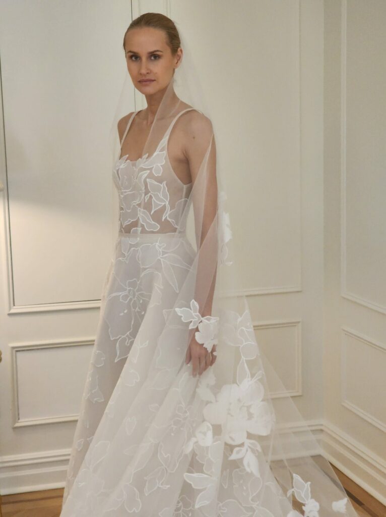 Woman in sheer floral wedding dress indoors.
