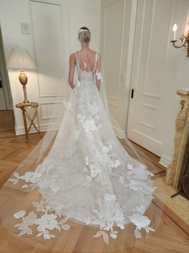 Bride in white gown and veil, facing away.