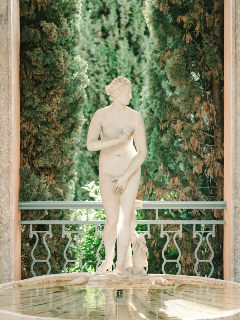 Marble nude statue by fountain in sunlit garden.