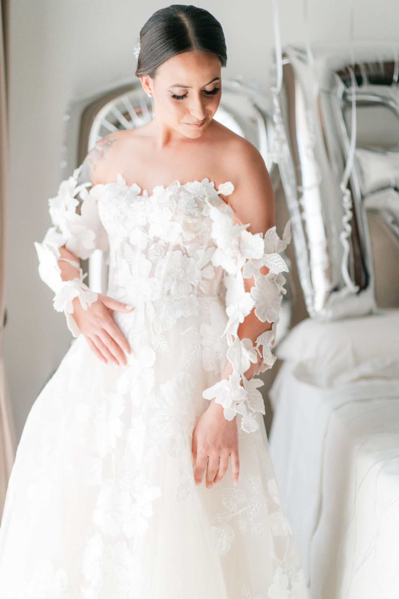 Bride in lace dress smiles near bed balloons.