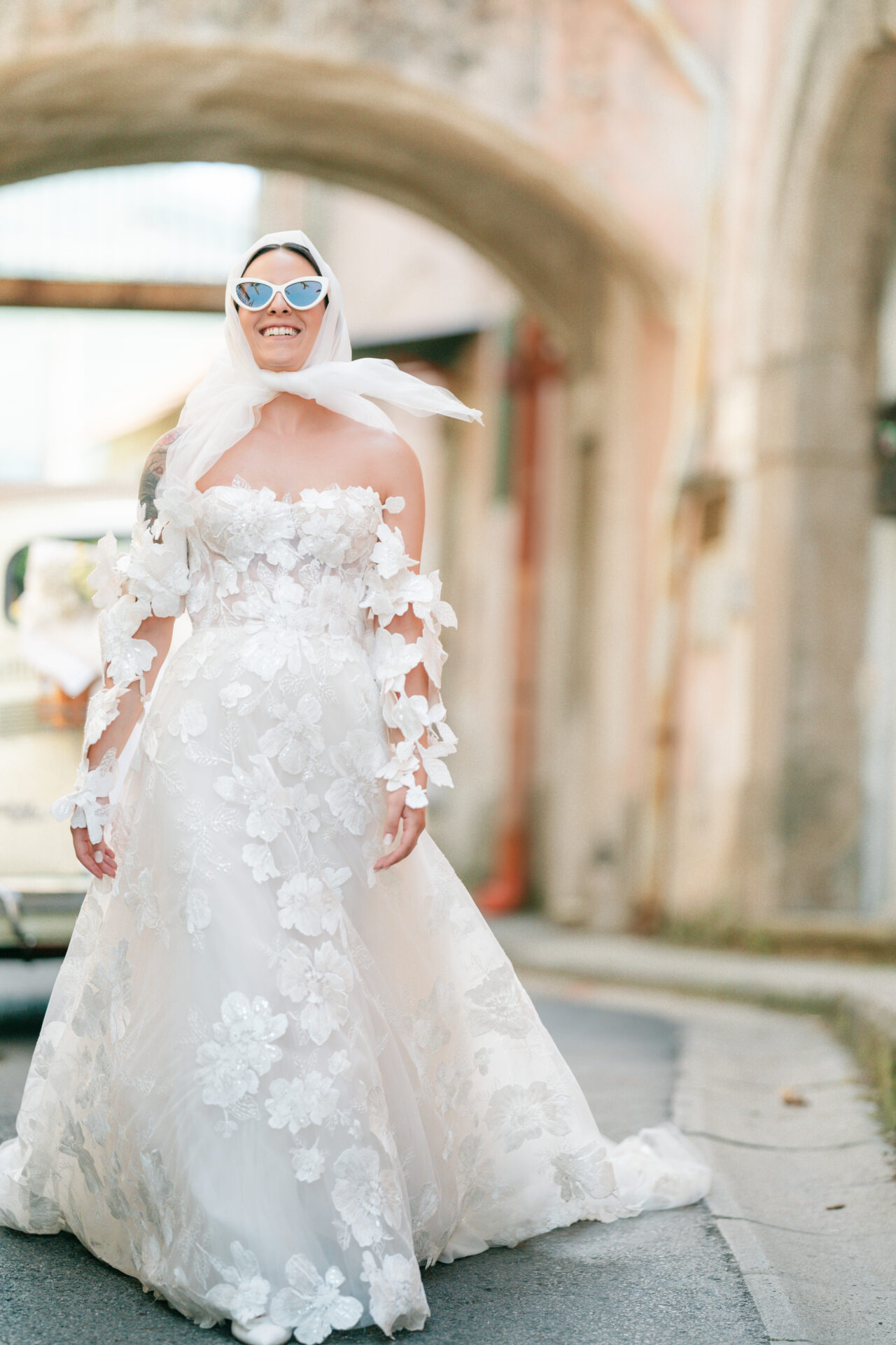 Smiling bride in white gown and sunglasses.