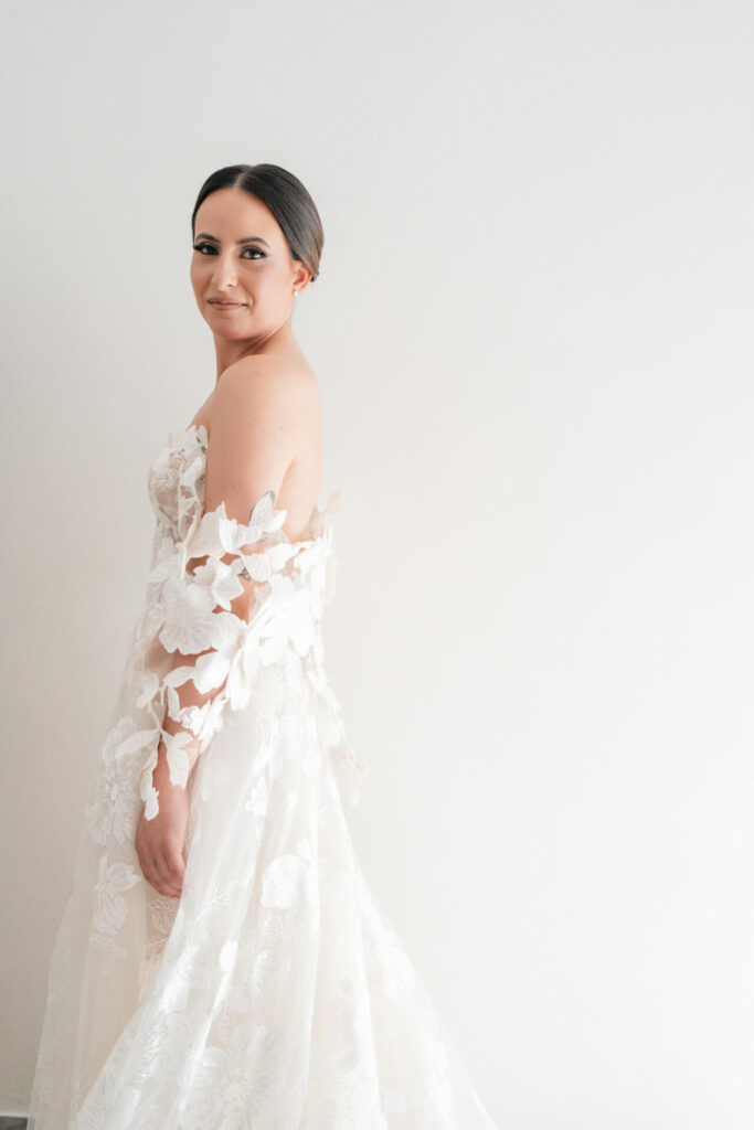 Woman in lace wedding dress smiles over shoulder.