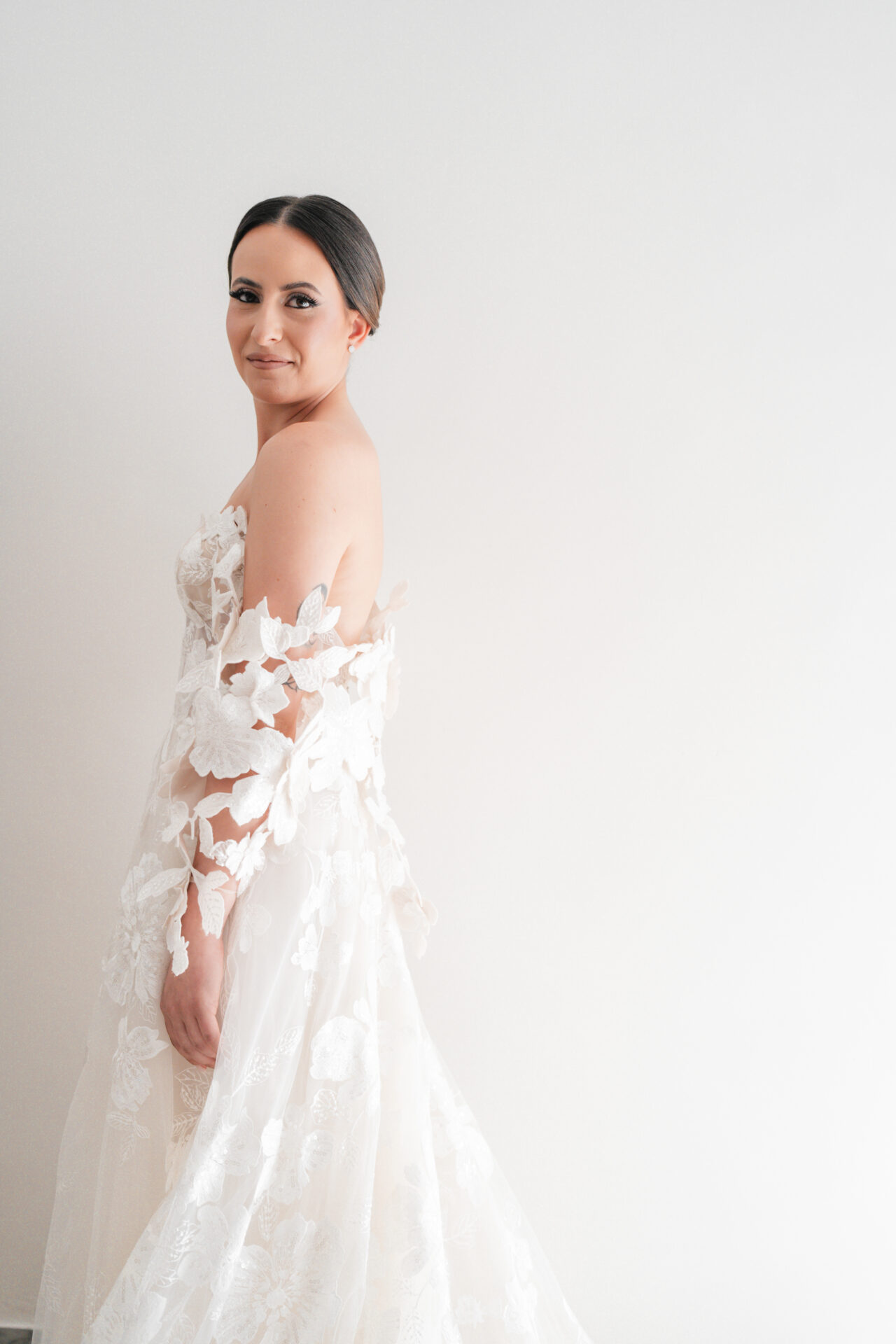 Woman in lace wedding dress smiles over shoulder.