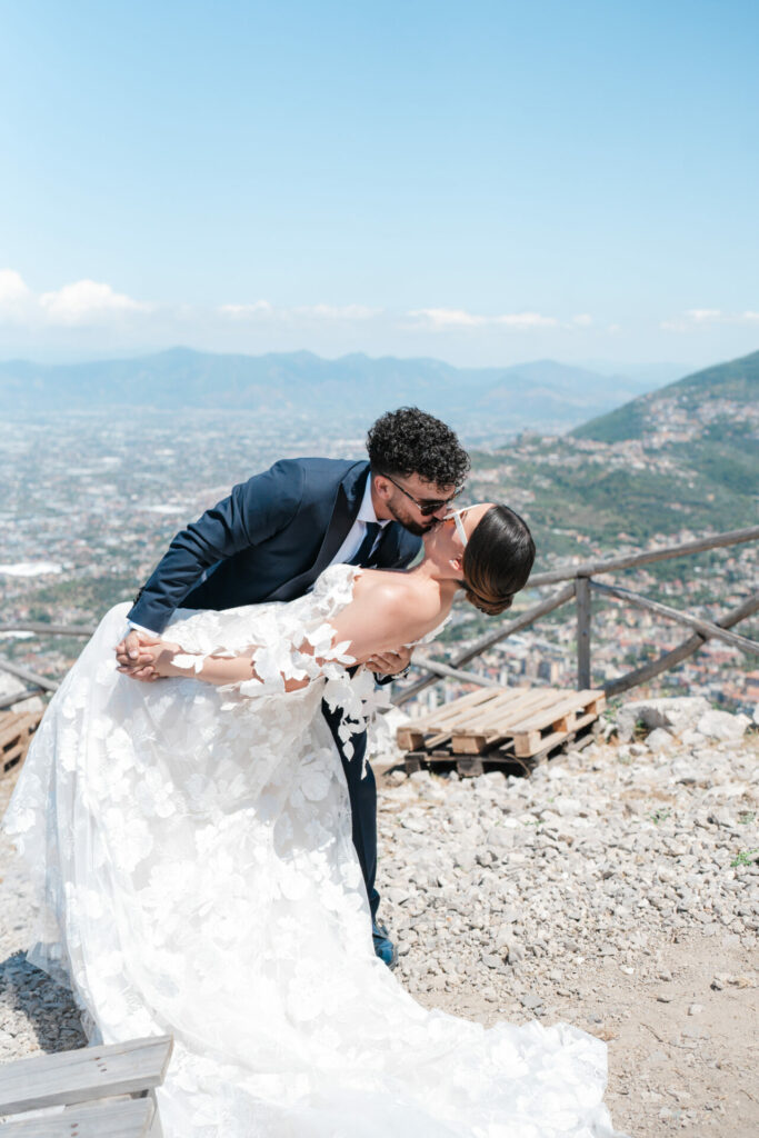 Groom dips bride atop hill with scenic view.