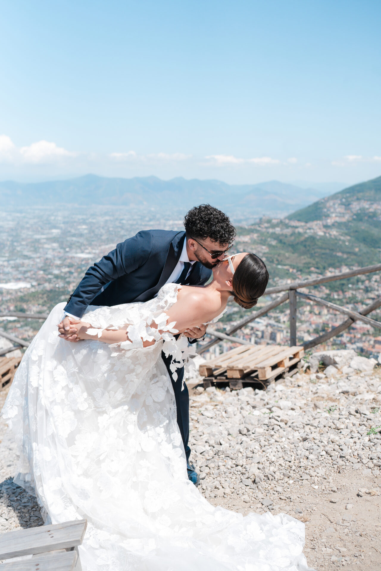 Groom dips bride atop hill with scenic view.