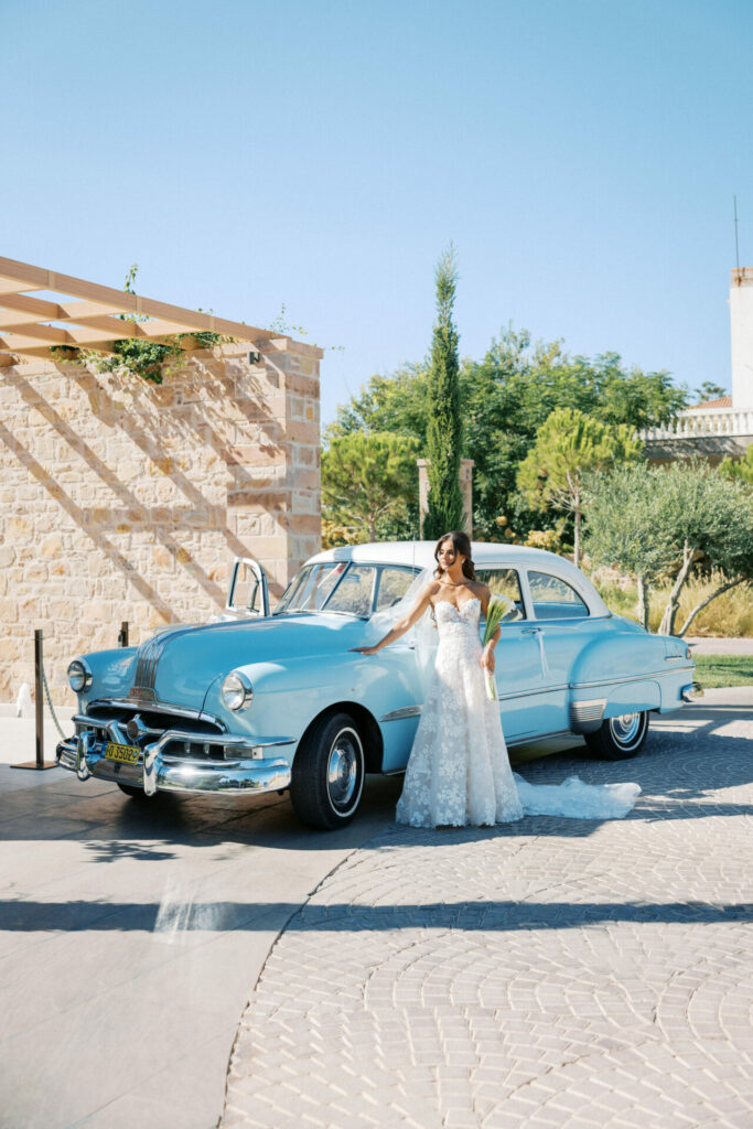 Katya Ruiz in couture gown by vintage blue car outside.
