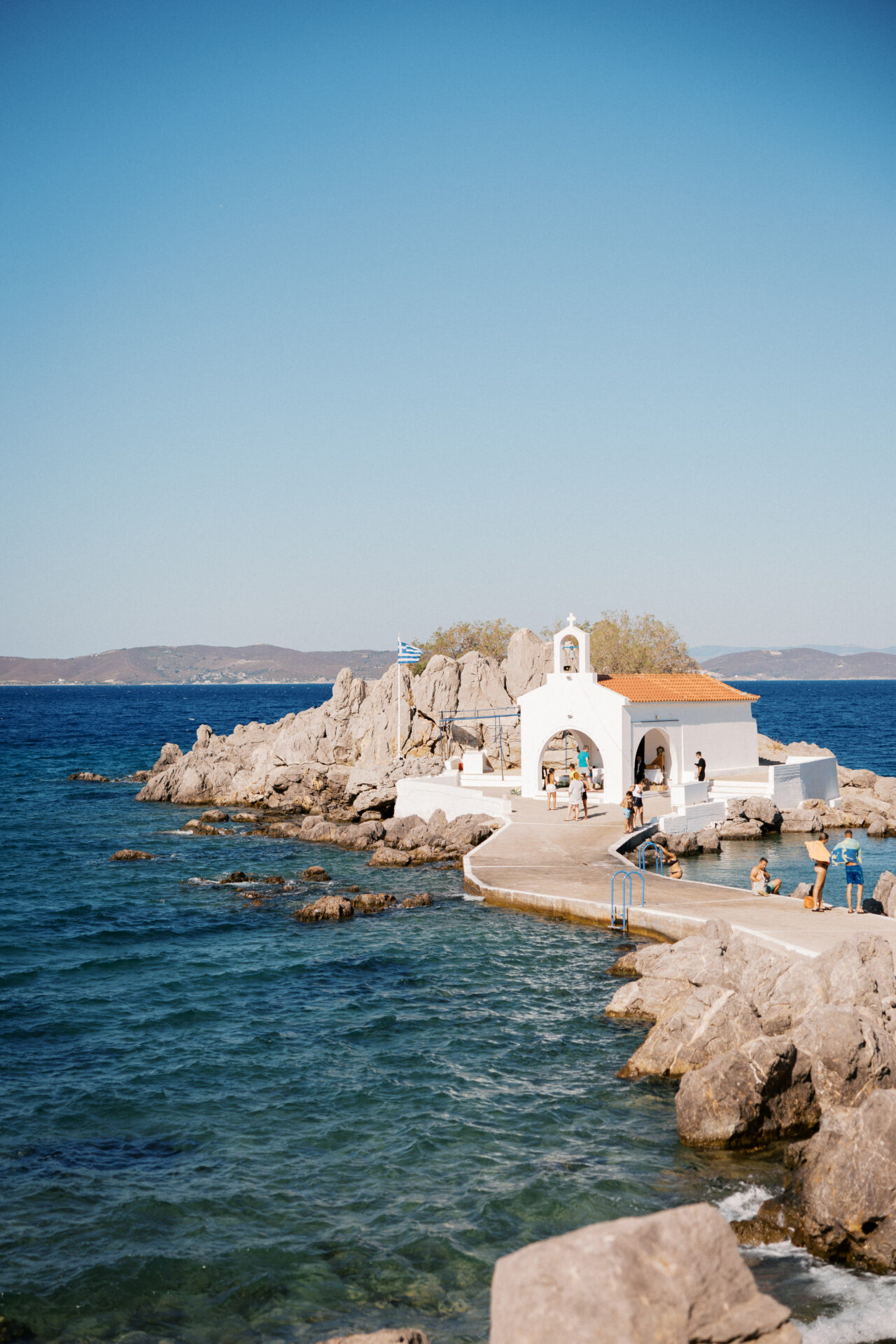 White chapel with red roof, Greek flag, seaside.