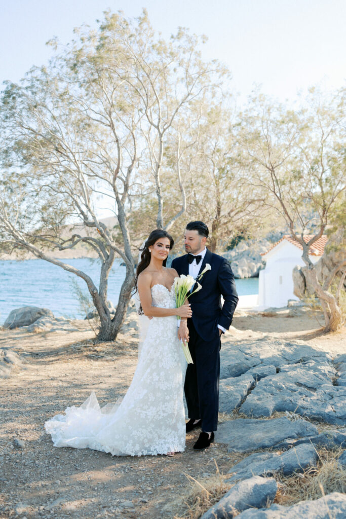 Bride in couture gown with groom, outdoors by water.