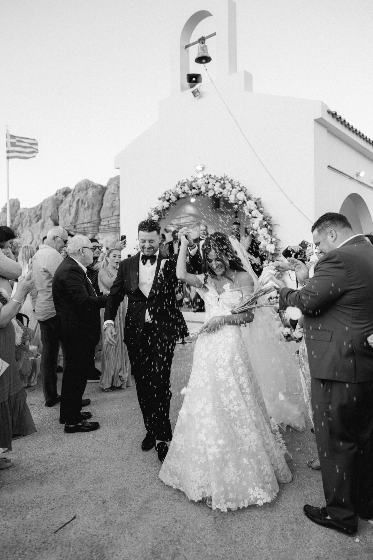 Bride and groom in couture exit chapel as confetti falls.