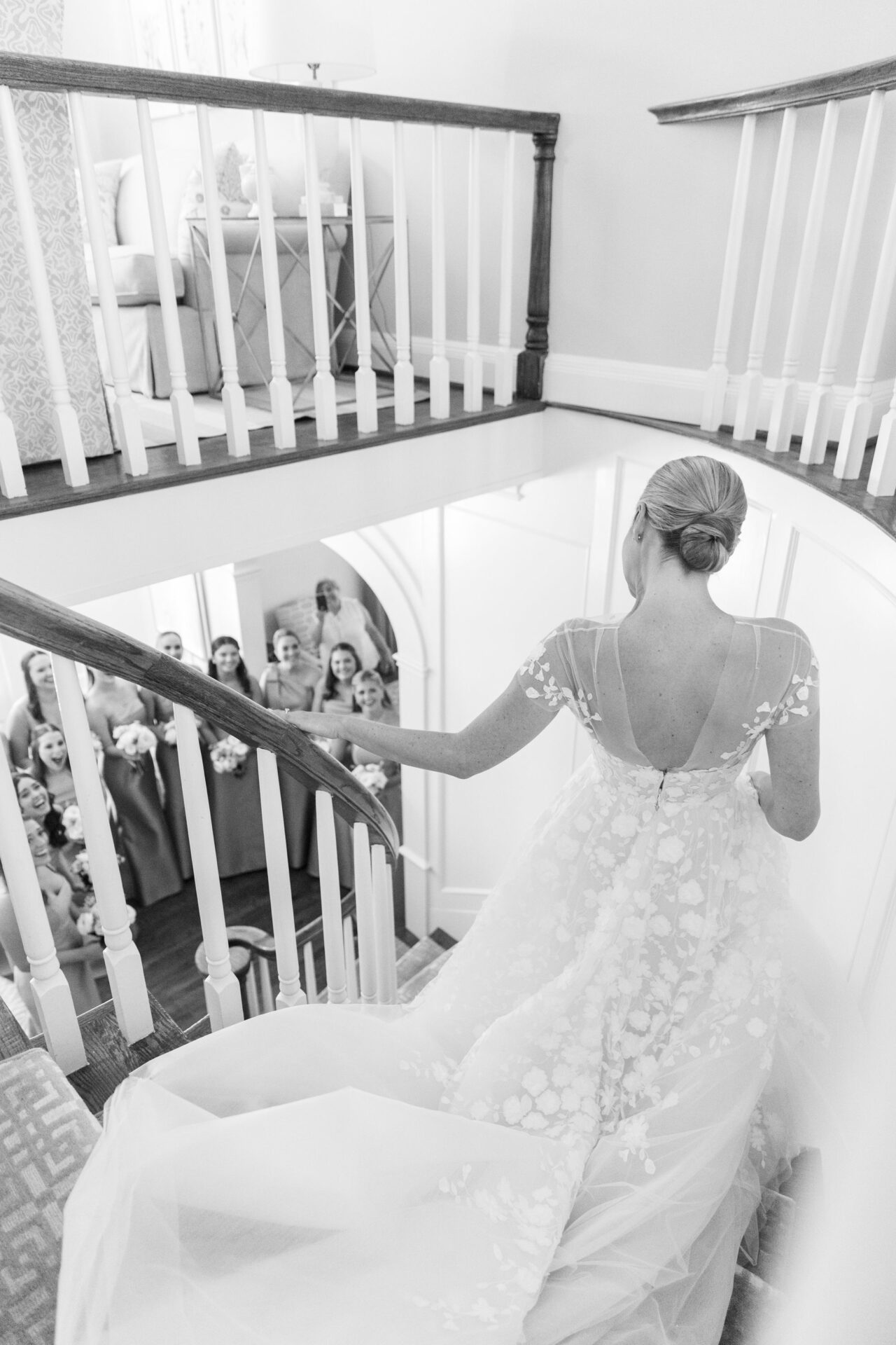 Bride descends stairs as bridesmaids watch, black and white.