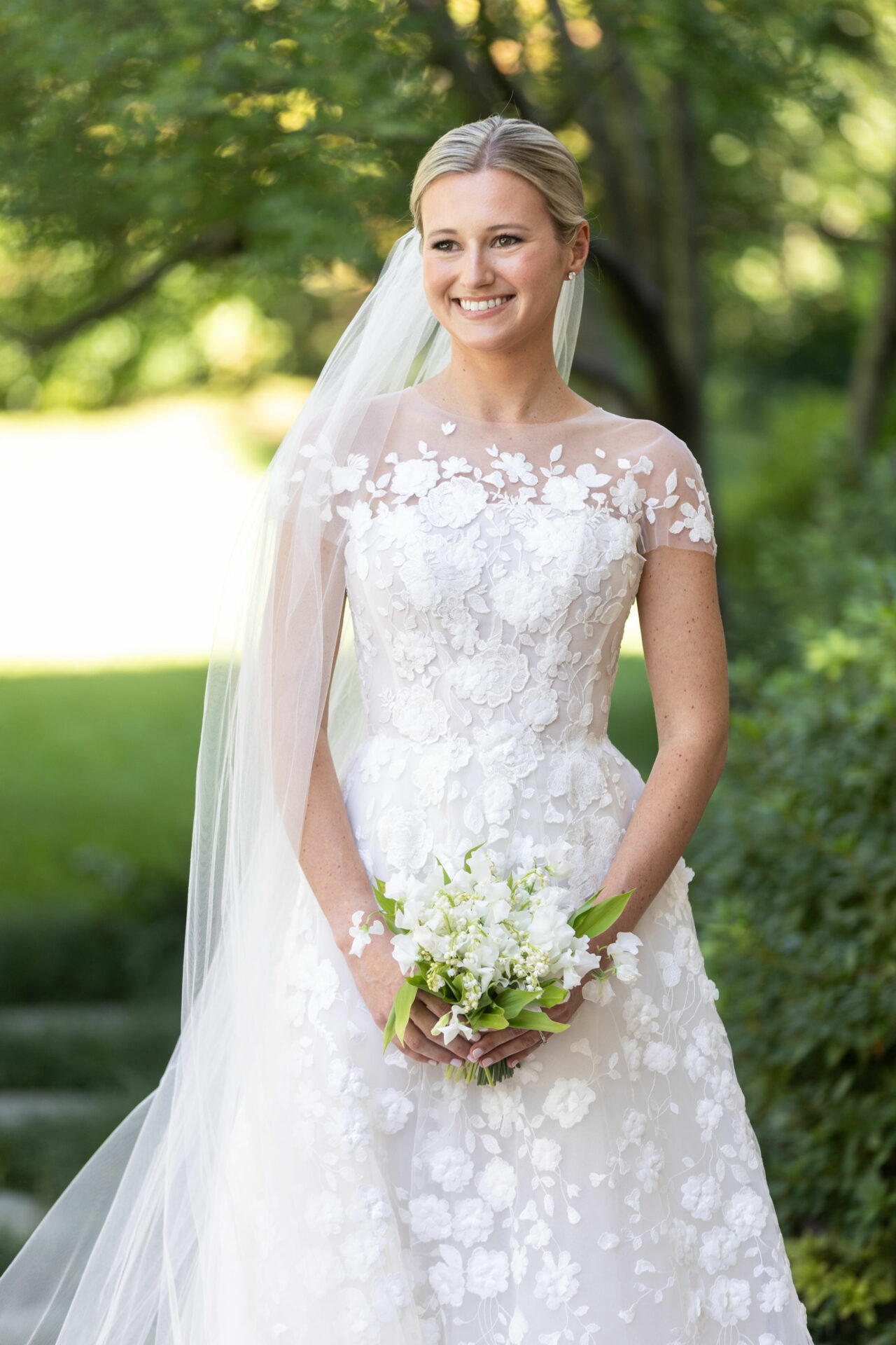 Bride in floral dress outdoors, smiling with bouquet.