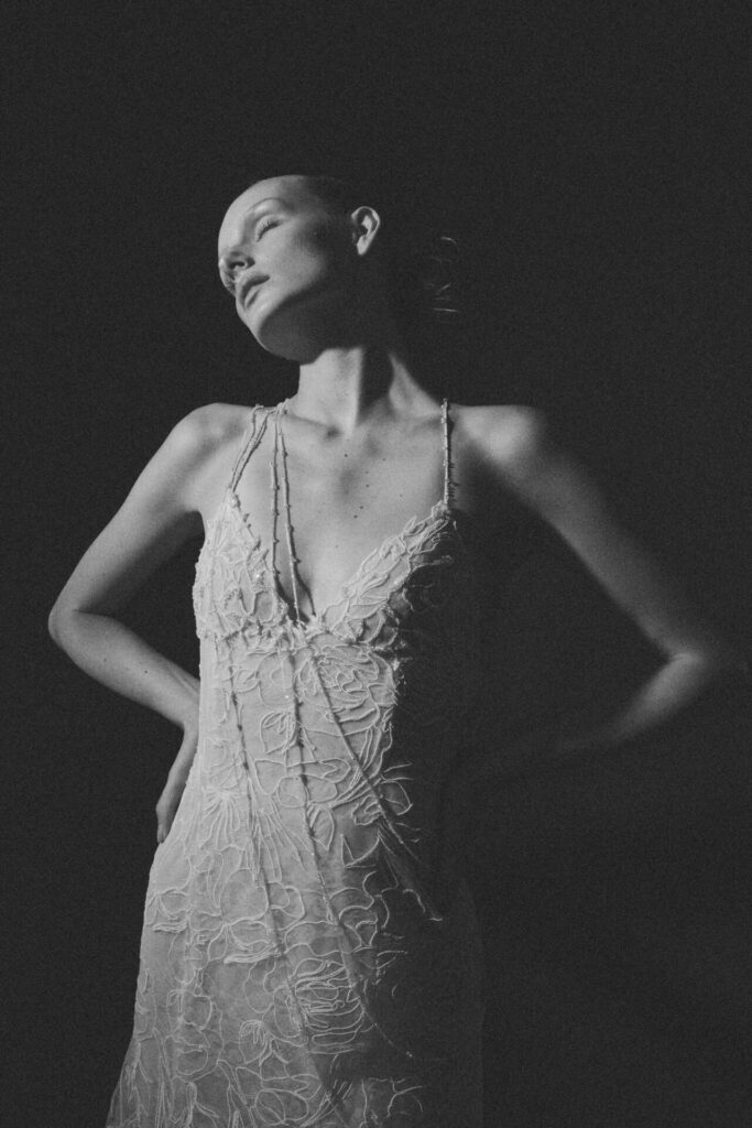 Woman in sleeveless dress poses under dramatic lighting.