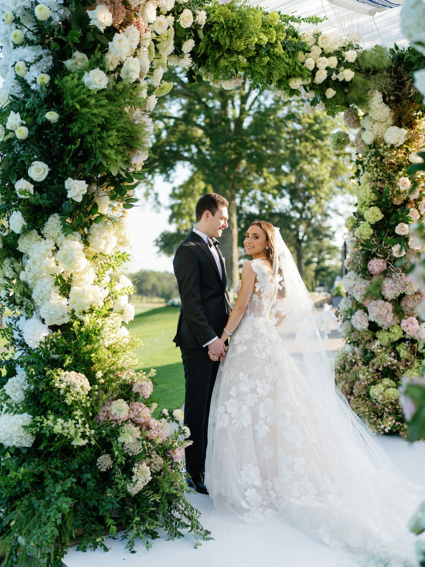 Bride and groom under floral arch, holding hands.