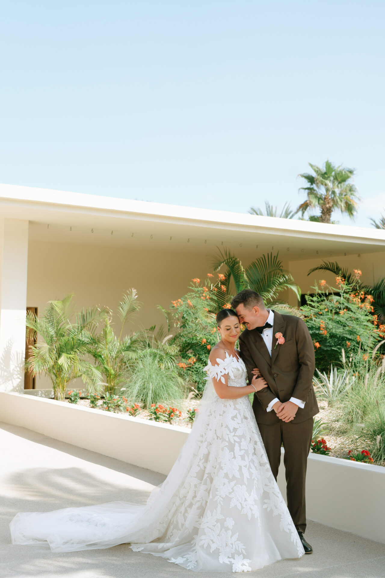 Bride and groom smile, touching foreheads in garden.