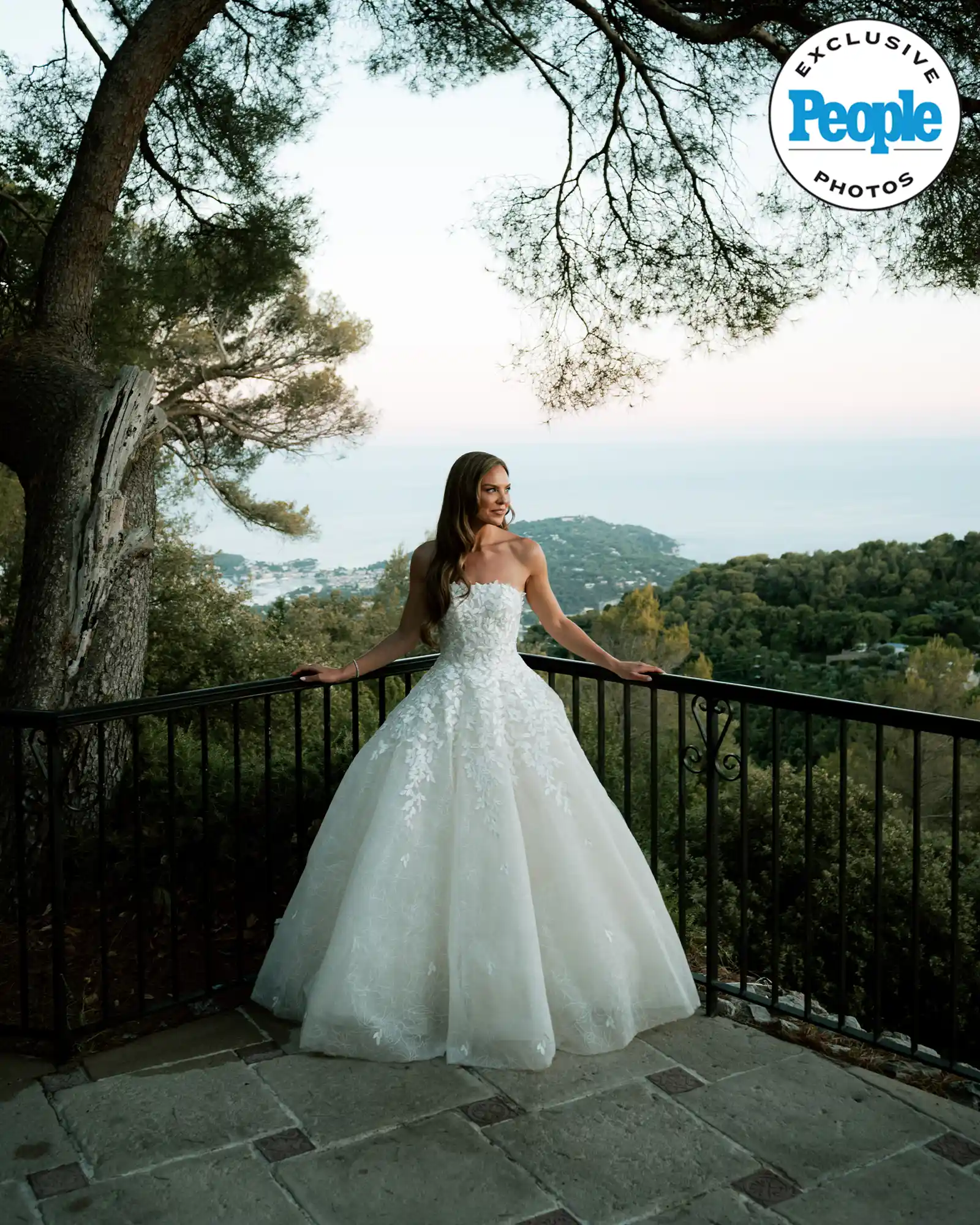 Bride in lace gown on terrace at sunset, ocean view.