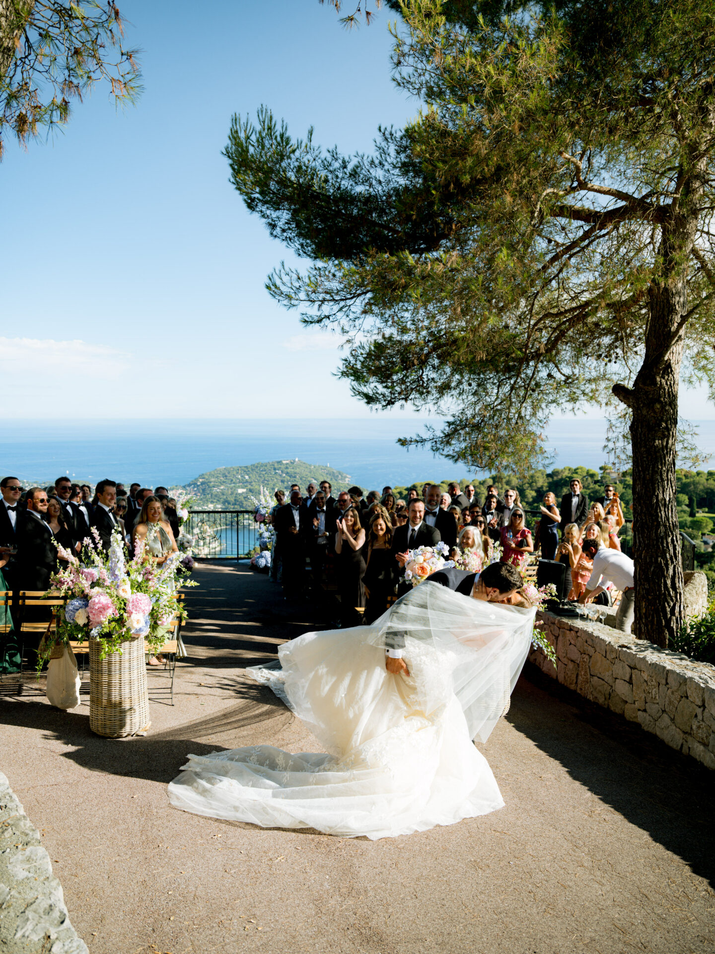 Bride and groom kiss outdoors with scenic backdrop.
