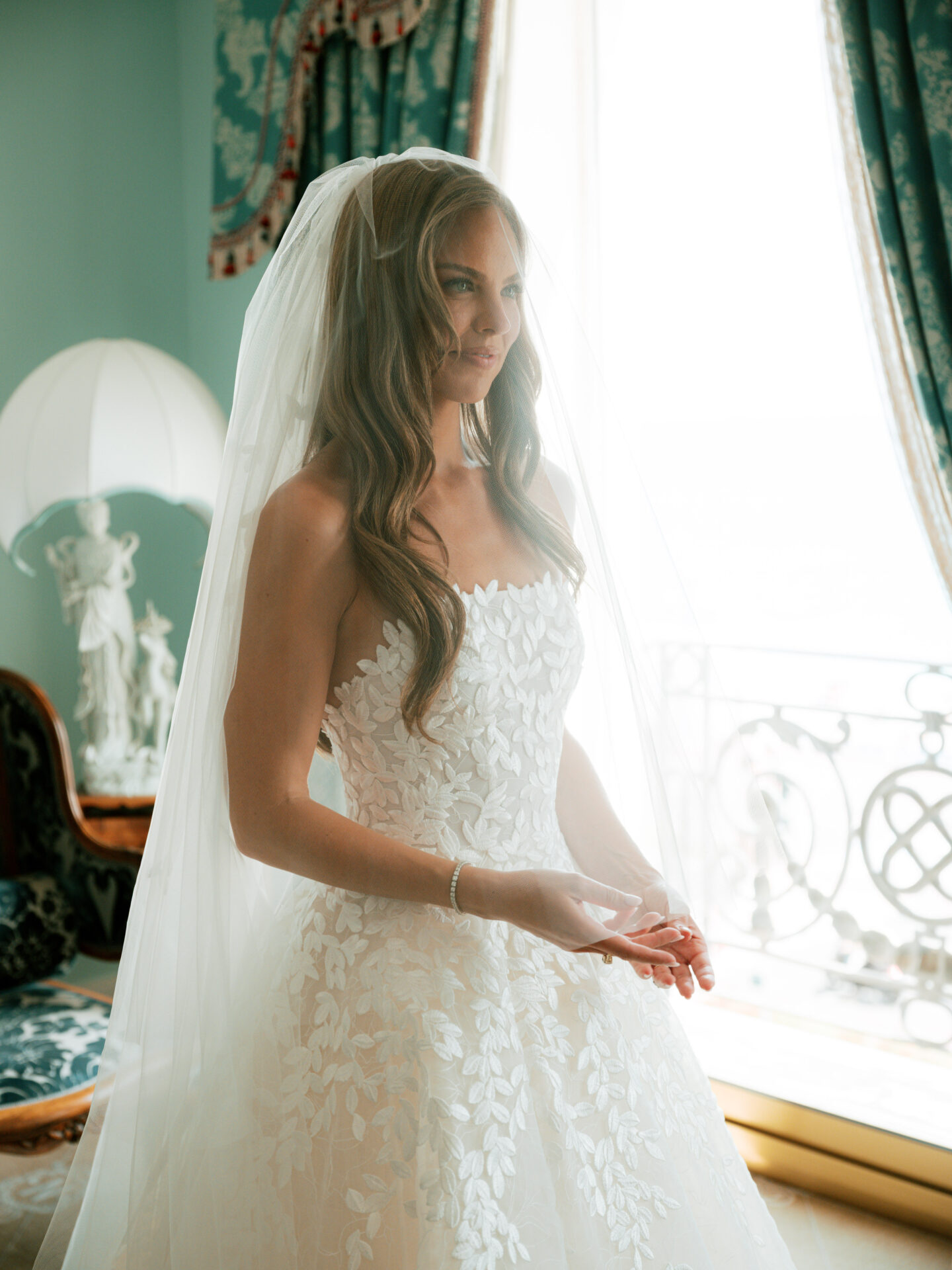 Bride in strapless gown by sunlit window indoors.