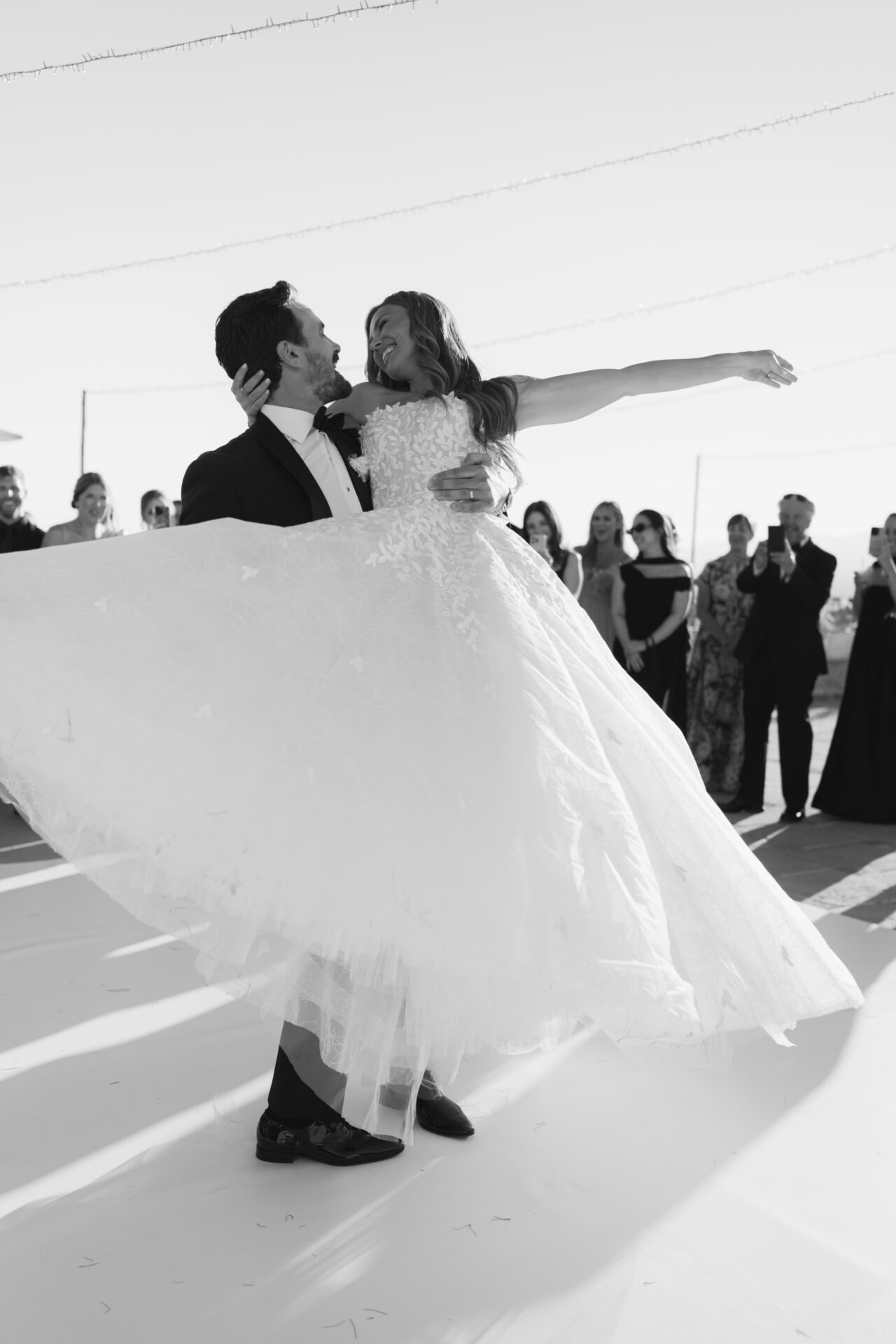 Groom lifts bride in first dance, guests watch.