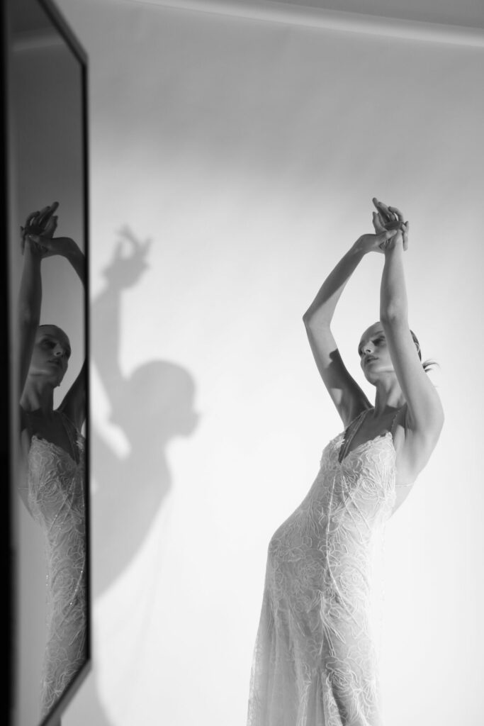 Woman in lace gown poses, shadow and reflection visible.