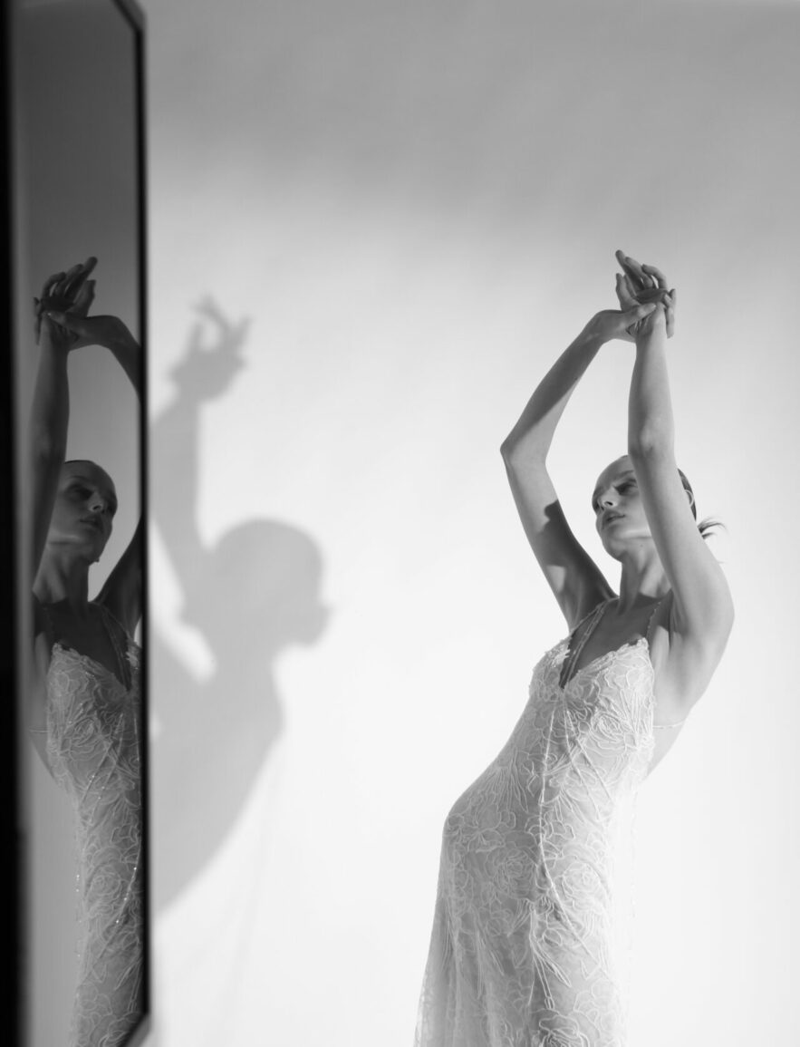 Woman in lace gown poses, shadow and reflection visible.